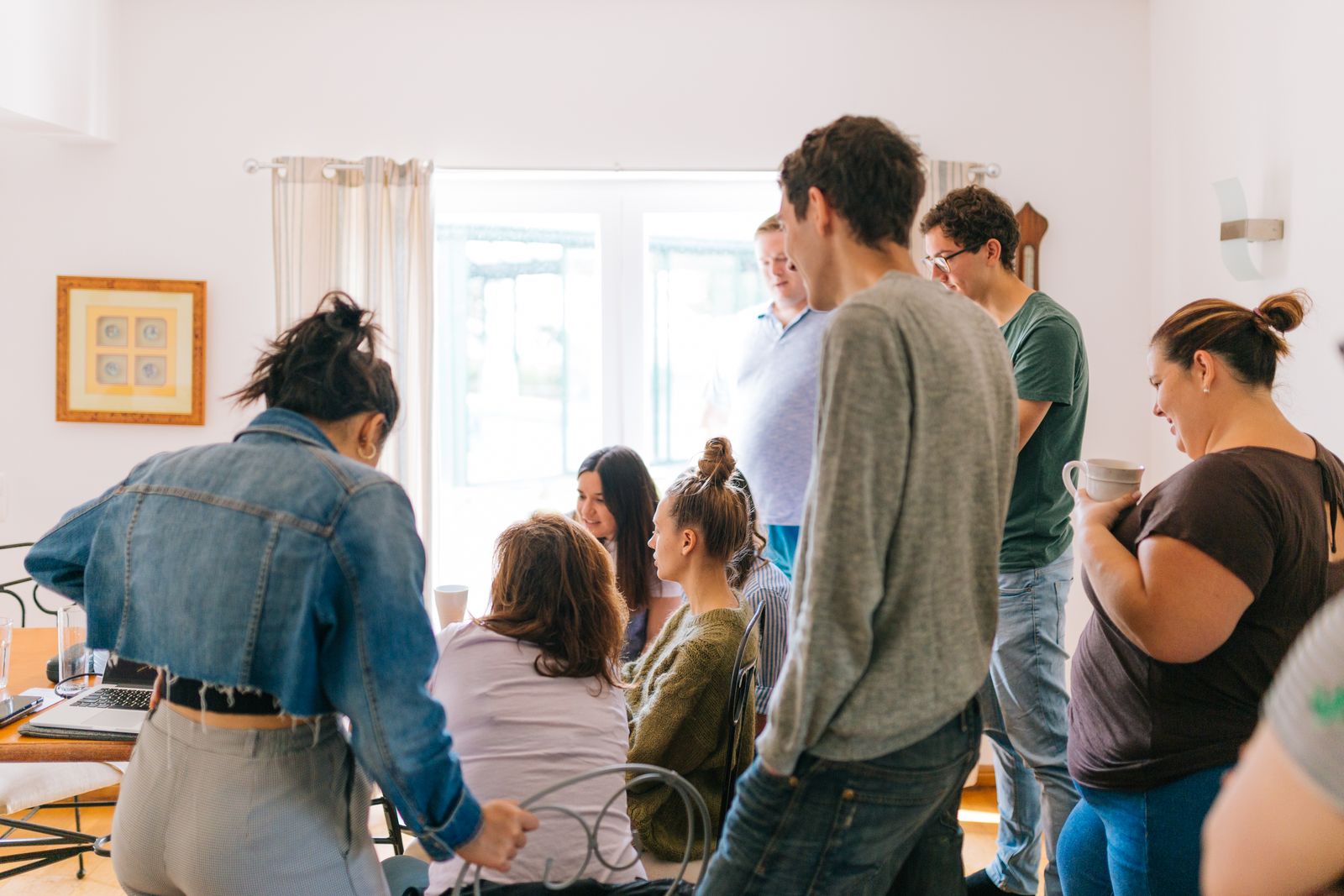 Grupo de pessoas reunidas em pé e sentadas ao redor de uma mesa com notebook durante um encontro informal.